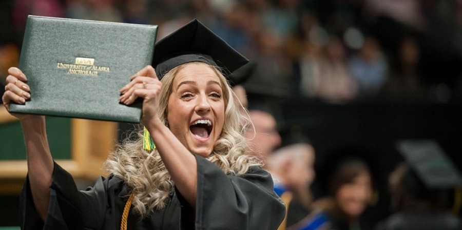 A UAA graduate holds up her diploma at the ceremony